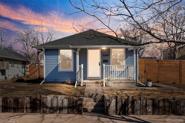 view of front facade with a fenced front yard, covered porch, and roof with shingles