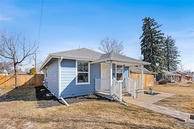 bungalow-style home with a front yard, a porch, fence, and roof with shingles