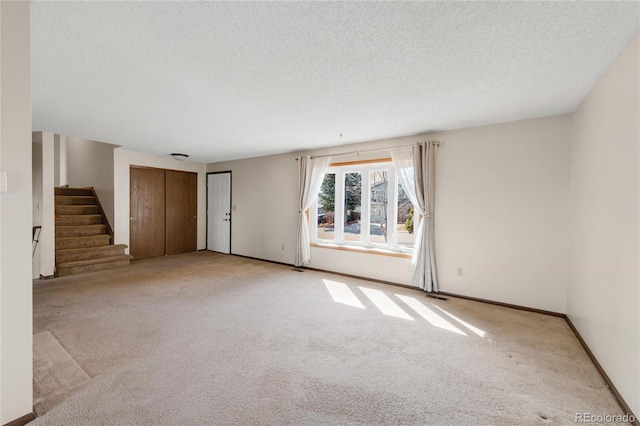 carpeted spare room featuring visible vents, baseboards, a textured ceiling, and stairs