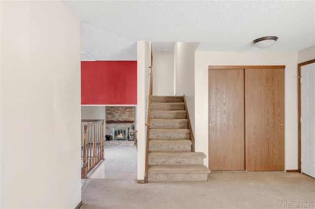 staircase featuring a textured ceiling, a fireplace, and carpet flooring