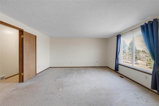 empty room with a textured ceiling, visible vents, baseboards, and light carpet