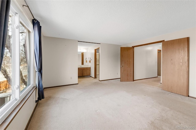 unfurnished bedroom with baseboards, light colored carpet, ensuite bathroom, and a textured ceiling