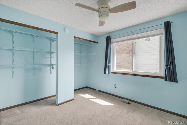 unfurnished bedroom with visible vents, multiple closets, a textured ceiling, carpet floors, and baseboards