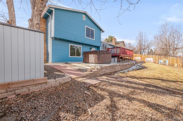 back of house featuring a wooden deck, fence, a lawn, and a hot tub