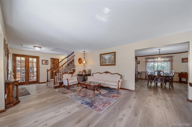 living area featuring a textured ceiling, french doors, a chandelier, light wood-style flooring, and stairs