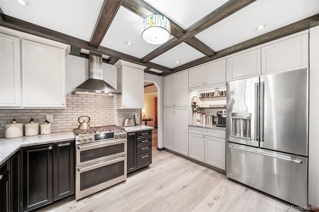 kitchen with stainless steel appliances, wall chimney range hood, backsplash, arched walkways, and light wood-style floors