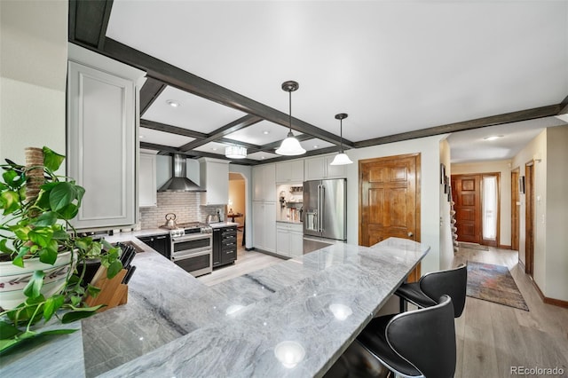 kitchen with stainless steel appliances, wall chimney exhaust hood, light wood finished floors, light stone countertops, and beam ceiling
