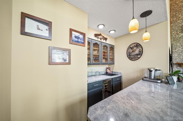 kitchen with glass insert cabinets, a sink, pendant lighting, a textured ceiling, and wine cooler