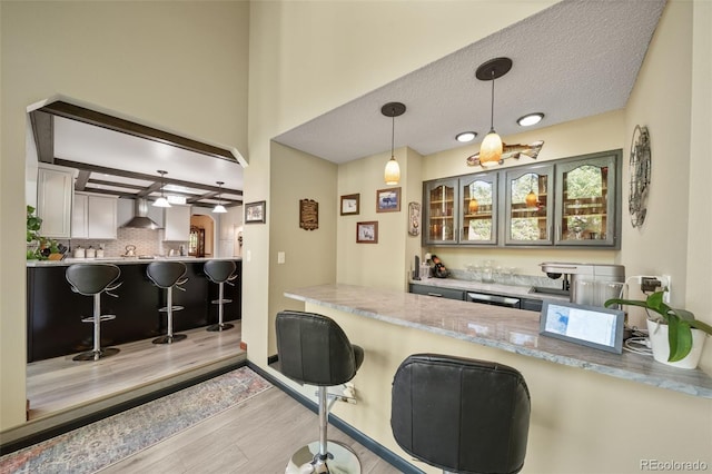 bar area with wall chimney exhaust hood, wood finished floors, pendant lighting, backsplash, and a textured ceiling