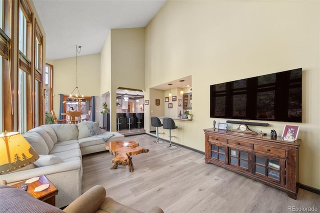 living area featuring a chandelier, wood finished floors, high vaulted ceiling, and baseboards
