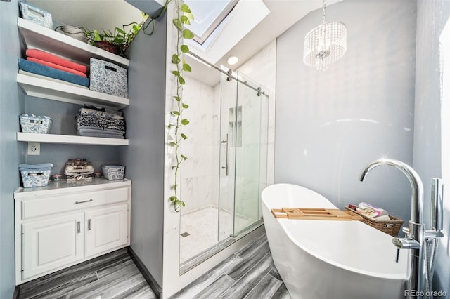 full bath featuring a skylight, a shower stall, a freestanding bath, wood finished floors, and a chandelier
