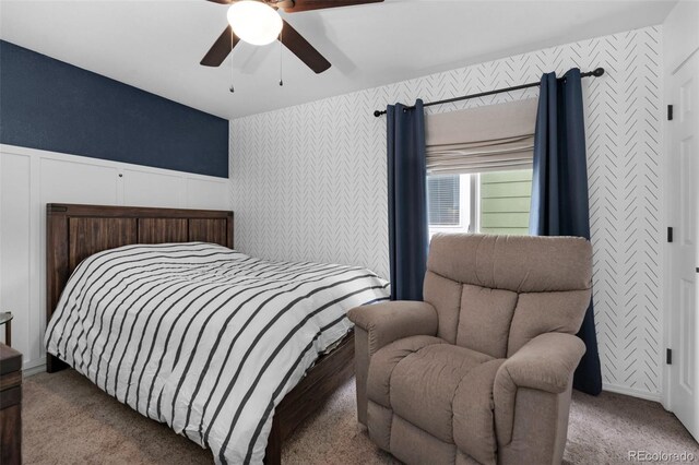 bedroom with carpet flooring, wallpapered walls, a wainscoted wall, and ceiling fan