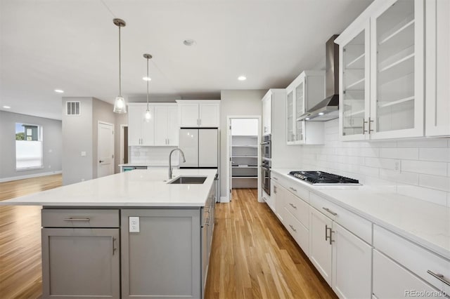 kitchen with white cabinets, stainless steel gas cooktop, wall chimney exhaust hood, and an island with sink