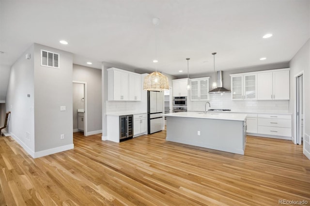 kitchen with white cabinets, beverage cooler, wall chimney range hood, and light hardwood / wood-style floors