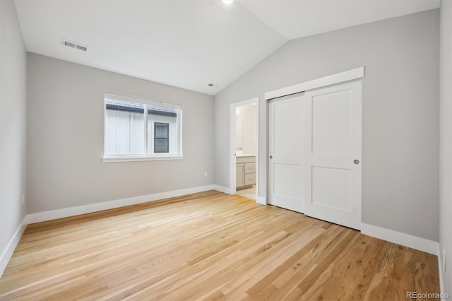 unfurnished bedroom featuring hardwood / wood-style floors, a closet, connected bathroom, and vaulted ceiling