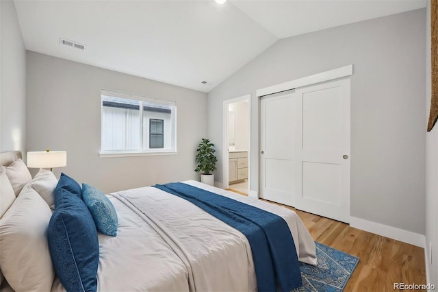 bedroom featuring hardwood / wood-style floors, ensuite bathroom, vaulted ceiling, and a closet