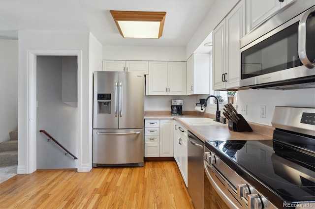 kitchen featuring light wood finished floors, white cabinets, appliances with stainless steel finishes, light countertops, and a sink