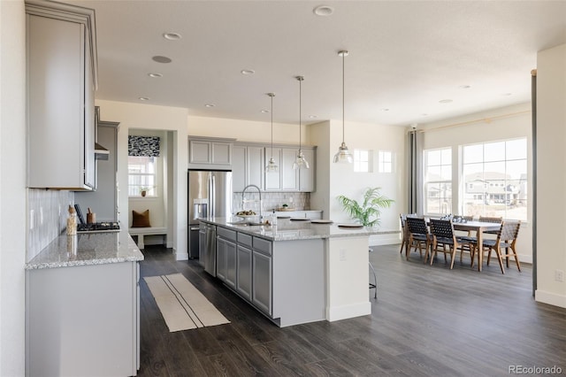 kitchen featuring sink, dark wood-type flooring, an island with sink, decorative light fixtures, and decorative backsplash