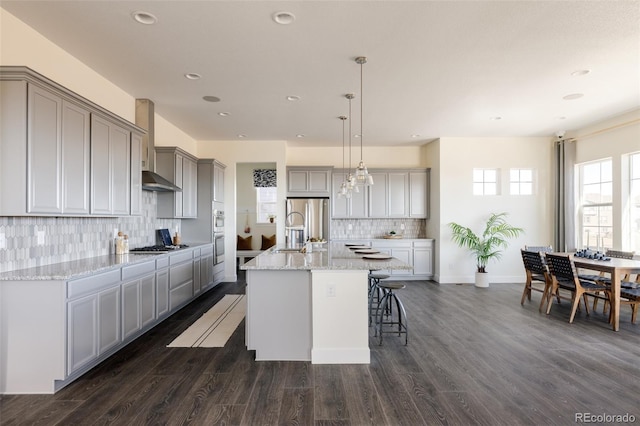 kitchen featuring wall chimney exhaust hood, dark hardwood / wood-style flooring, an island with sink, and tasteful backsplash