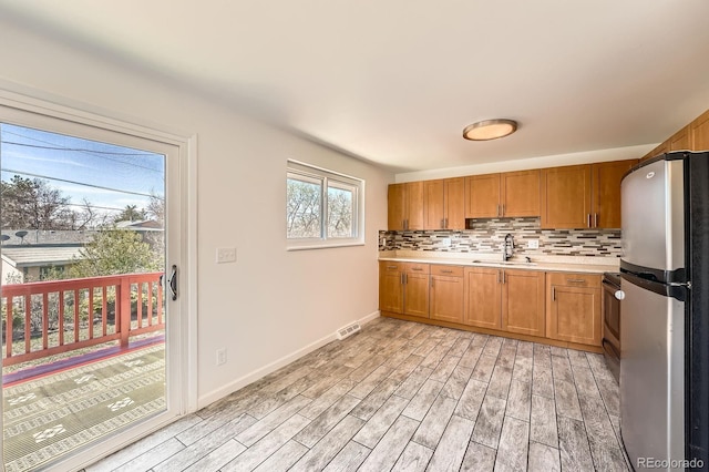 13086 E Alaska Ave, Aurora, CO 80012 - kitchen featuring freestanding refrigerator, light countertops, light wood finished floors, tasteful backsplash, and brown cabinets