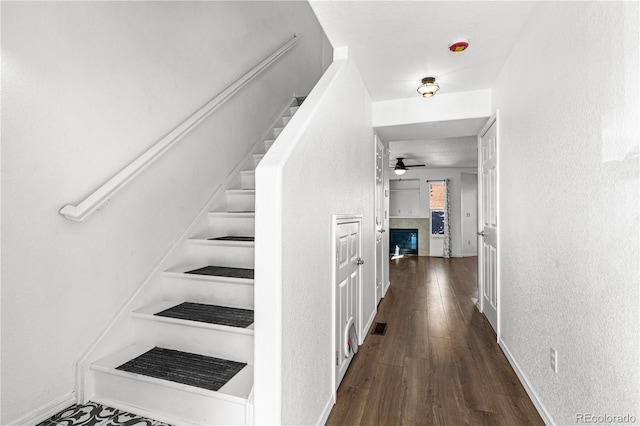 stairs featuring wood finished floors, visible vents, a textured wall, and ceiling fan