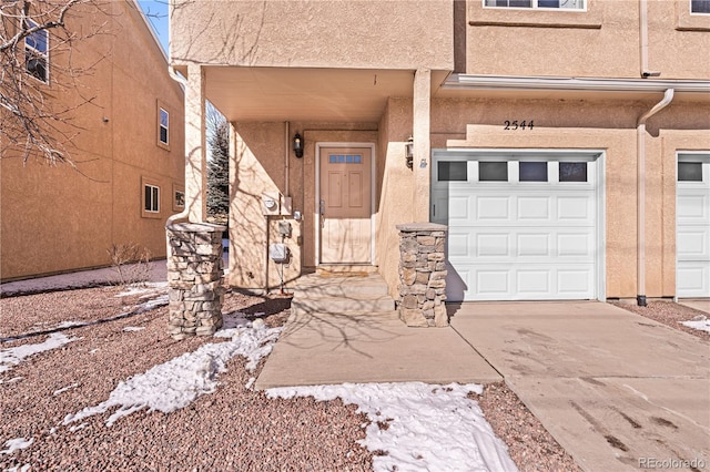 entrance to property with stucco siding, an attached garage, and driveway