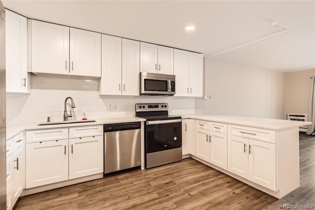 kitchen featuring white cabinets, appliances with stainless steel finishes, a peninsula, light wood-type flooring, and a sink