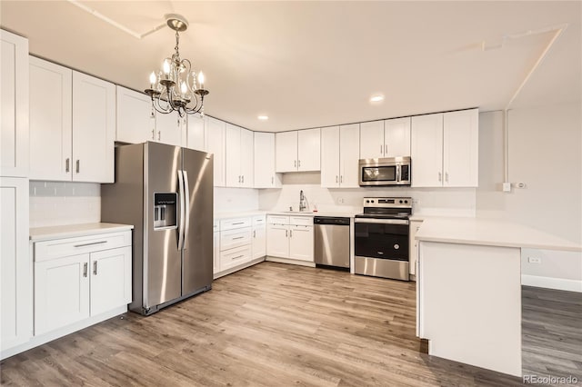 kitchen featuring a notable chandelier, appliances with stainless steel finishes, a sink, light wood-type flooring, and a peninsula