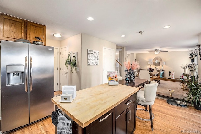 kitchen featuring butcher block counters, a breakfast bar area, light hardwood / wood-style flooring, stainless steel fridge with ice dispenser, and ceiling fan