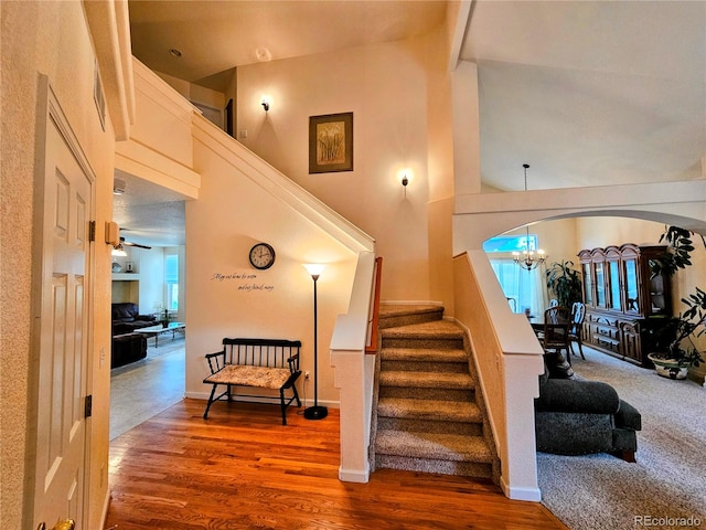 stairs featuring hardwood / wood-style flooring, ceiling fan with notable chandelier, and vaulted ceiling