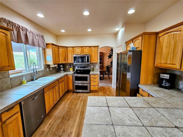 kitchen with backsplash, tile countertops, light hardwood / wood-style flooring, sink, and stainless steel appliances