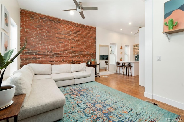 living room with brick wall, wood finished floors, visible vents, and baseboards