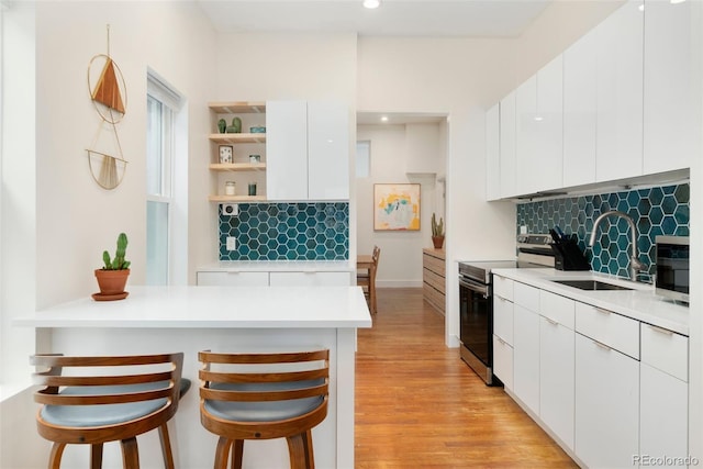 kitchen with modern cabinets, a breakfast bar area, stainless steel range with electric stovetop, open shelves, and a sink