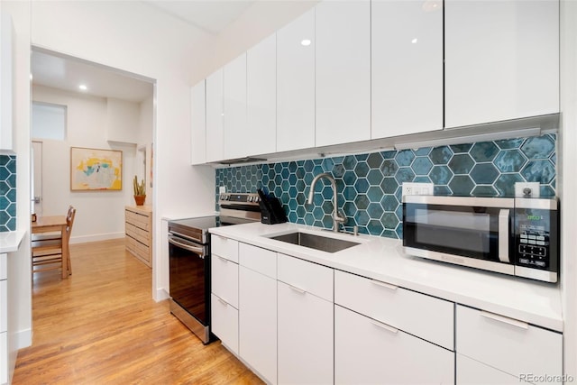 kitchen featuring white cabinets, light wood-style flooring, stainless steel appliances, light countertops, and a sink