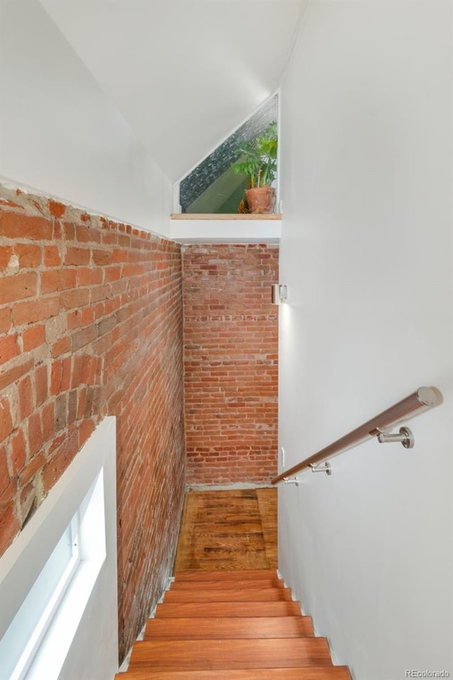 stairway with lofted ceiling, brick wall, and wood finished floors