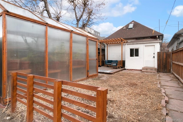 exterior space featuring a shingled roof, a greenhouse, fence, and an outdoor structure