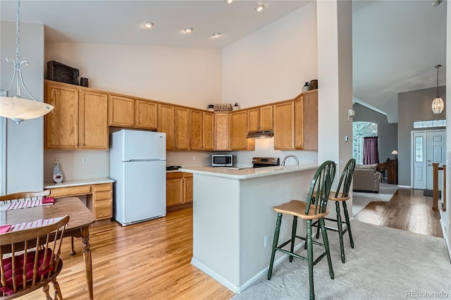 kitchen featuring stainless steel appliances, light wood-type flooring, hanging light fixtures, kitchen peninsula, and high vaulted ceiling