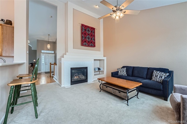 living room featuring a tile fireplace, ceiling fan, and carpet