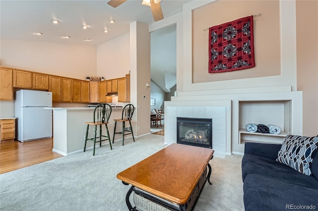 living room with a tiled fireplace, light colored carpet, ceiling fan, and a high ceiling