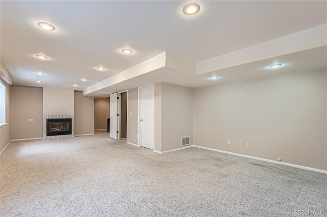 basement featuring a tiled fireplace and light colored carpet