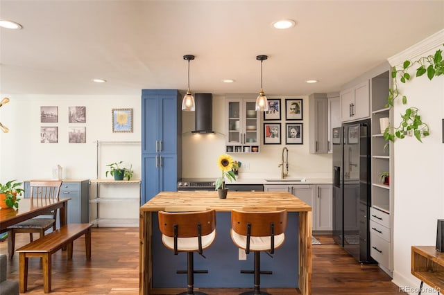 kitchen featuring stainless steel refrigerator with ice dispenser, dark hardwood / wood-style floors, decorative light fixtures, wall chimney range hood, and sink