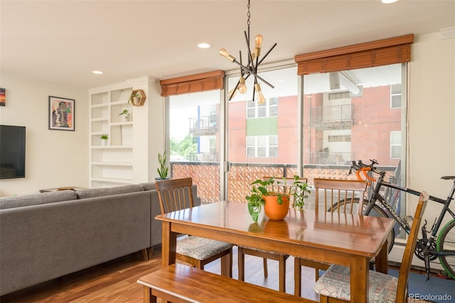 dining room with wood-type flooring, built in features, crown molding, and a chandelier