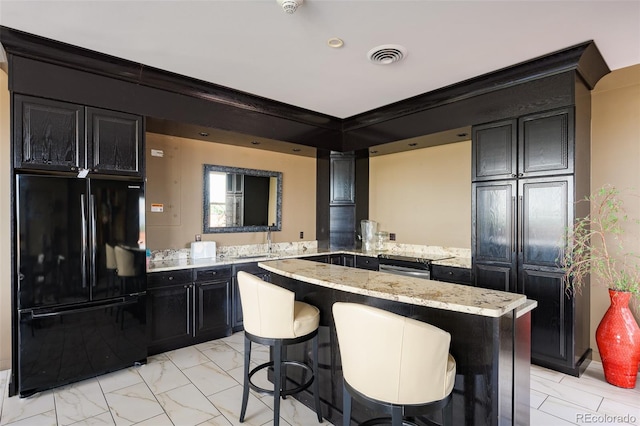 kitchen featuring kitchen peninsula, a breakfast bar area, black fridge, light stone countertops, and sink