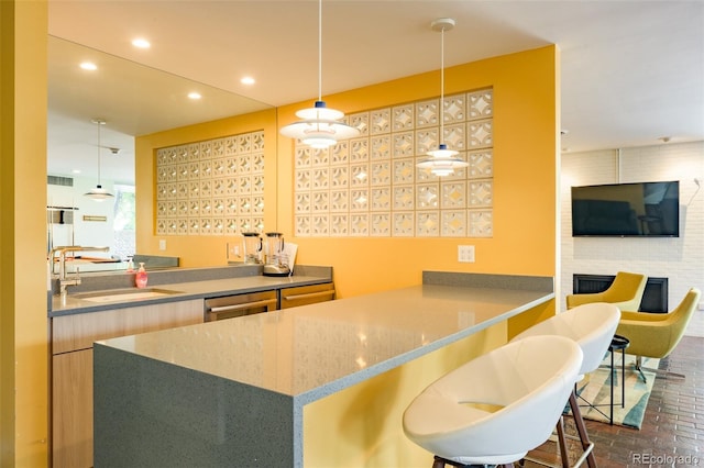 kitchen featuring dishwasher, decorative light fixtures, sink, kitchen peninsula, and a brick fireplace