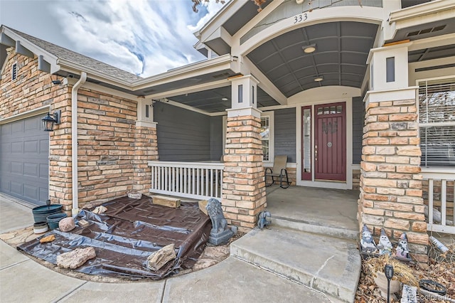 doorway to property with a shingled roof, covered porch, brick siding, and a garage