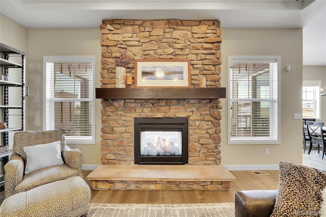 living area featuring wood finished floors, baseboards, and a stone fireplace