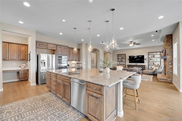 kitchen with appliances with stainless steel finishes, a sink, arched walkways, a ceiling fan, and an island with sink
