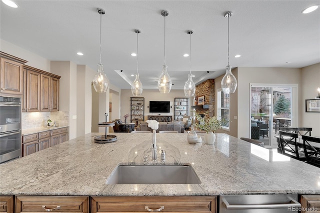 kitchen featuring double oven, a sink, open floor plan, a center island with sink, and light stone counters