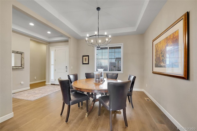 dining space featuring a tray ceiling, light wood finished floors, a chandelier, and recessed lighting