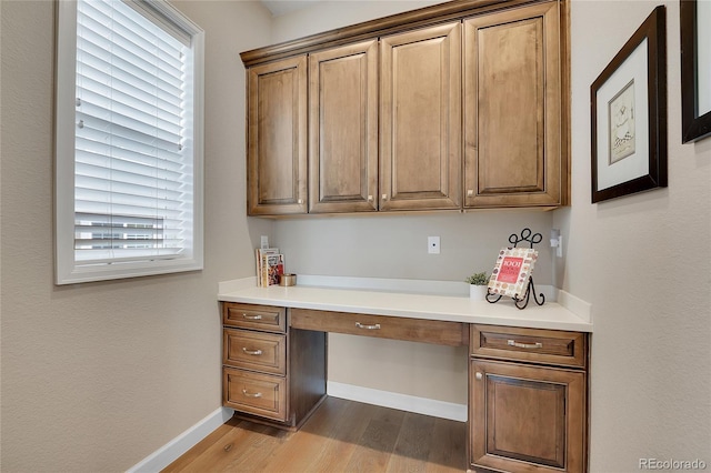 home office featuring built in study area, dark wood-type flooring, and baseboards
